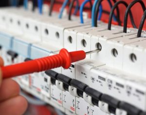 Hand of an electrician with multimeter probe at an electrical sw